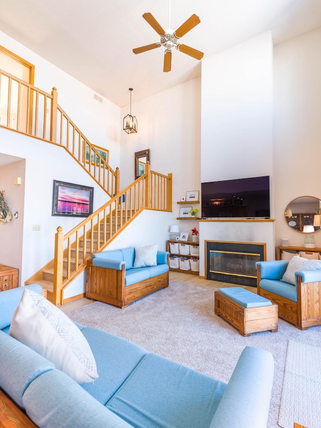 living area with stairs, visible vents, a towering ceiling, and ceiling fan