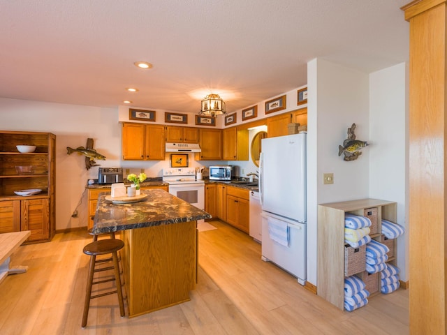 kitchen with white appliances, light wood finished floors, under cabinet range hood, and a center island