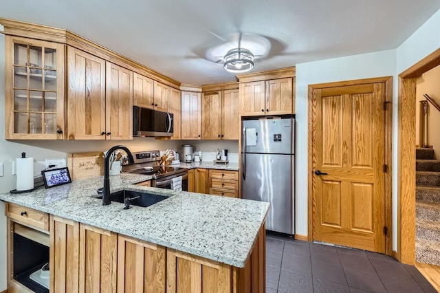 kitchen featuring a sink, appliances with stainless steel finishes, a peninsula, glass insert cabinets, and light stone countertops