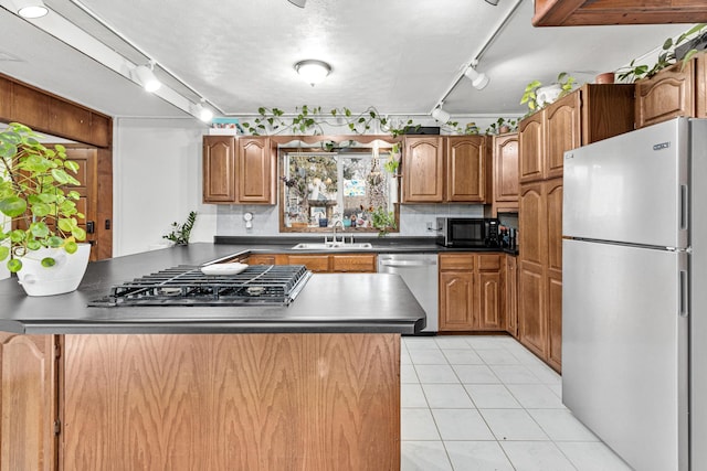 kitchen with brown cabinets, dark countertops, tasteful backsplash, appliances with stainless steel finishes, and light tile patterned flooring