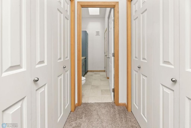 hallway with baseboards, light colored carpet, and light tile patterned flooring