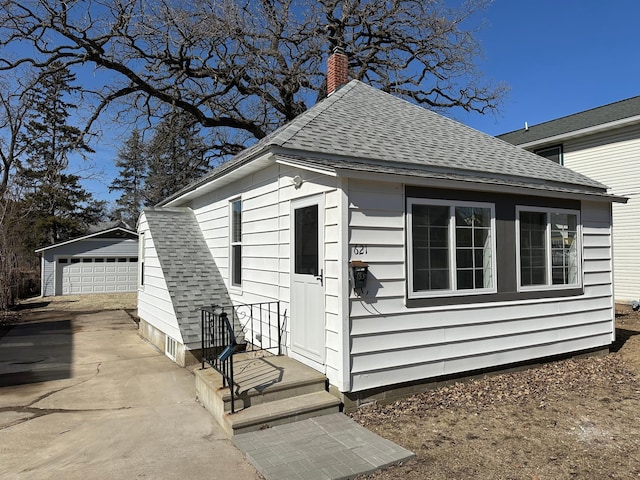 view of side of home with an outdoor structure, a chimney, a detached garage, and a shingled roof