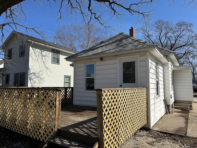 exterior space with roof with shingles, a deck, and a chimney