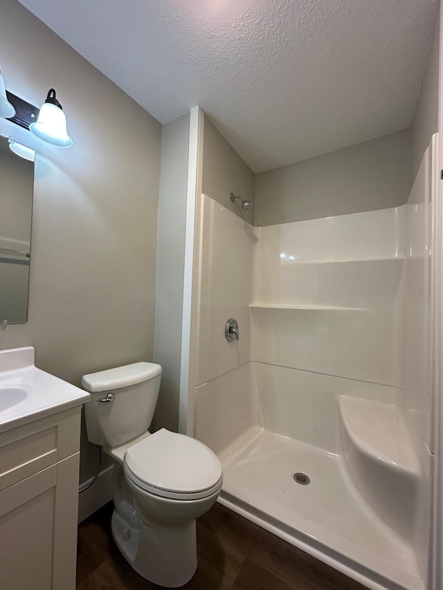 full bath with toilet, a textured ceiling, wood finished floors, walk in shower, and vanity