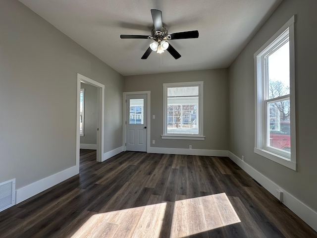 empty room with visible vents, plenty of natural light, dark wood-style floors, and baseboards