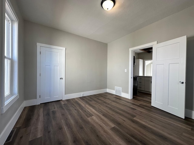 unfurnished bedroom with dark wood finished floors, visible vents, multiple windows, and baseboards