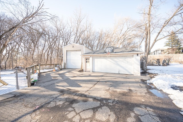 snow covered garage with a detached garage and fence