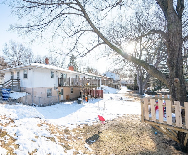 snow covered back of property featuring a wooden deck, a chimney, and fence