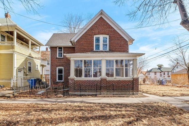 view of front of property featuring brick siding, a shingled roof, fence, and a sunroom