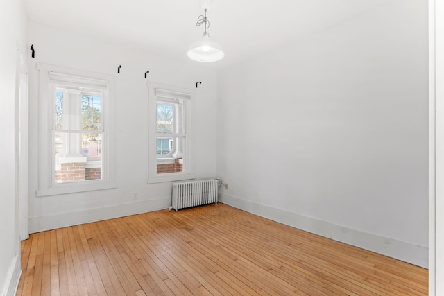 empty room with light wood finished floors, radiator heating unit, and baseboards