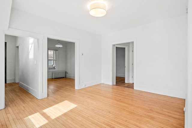 unfurnished room with light wood-type flooring, baseboards, and radiator heating unit