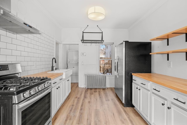 kitchen with open shelves, radiator heating unit, stacked washer / drying machine, appliances with stainless steel finishes, and butcher block counters