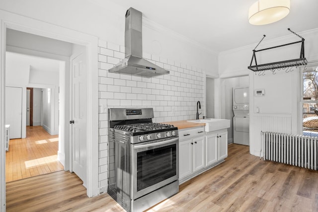 kitchen with radiator heating unit, stainless steel range with gas stovetop, a sink, stacked washer / dryer, and exhaust hood