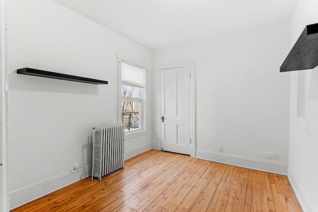 unfurnished bedroom with radiator heating unit, baseboards, and wood-type flooring