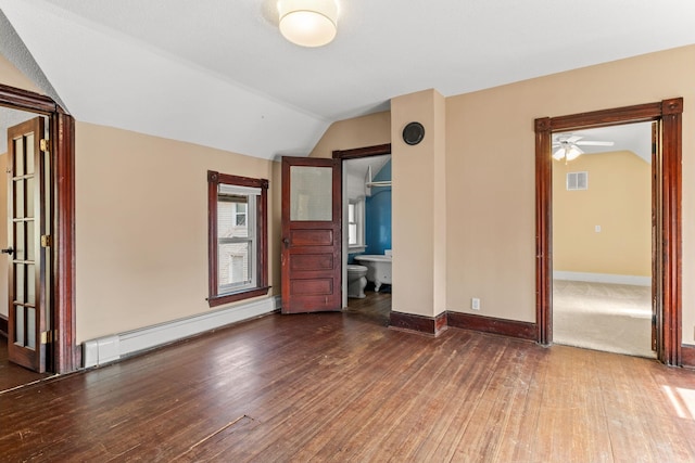 empty room featuring visible vents, a baseboard heating unit, baseboards, vaulted ceiling, and wood-type flooring