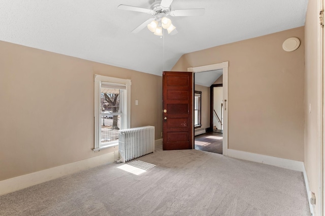 carpeted spare room featuring radiator, baseboards, a ceiling fan, and vaulted ceiling