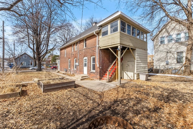 back of house featuring brick siding, a chimney, and a garden