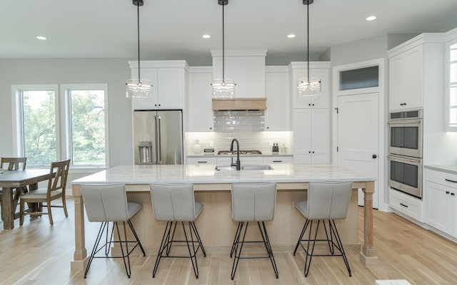 kitchen with light wood finished floors, a sink, stainless steel appliances, white cabinets, and tasteful backsplash