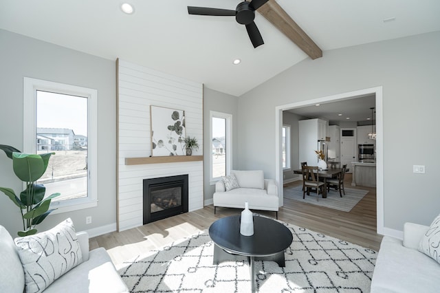 living room featuring lofted ceiling with beams, a fireplace, light wood-style floors, and baseboards