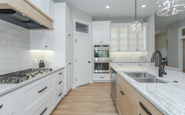 kitchen with light wood finished floors, a sink, custom range hood, glass insert cabinets, and appliances with stainless steel finishes