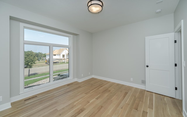 empty room with light wood-style floors, visible vents, and baseboards