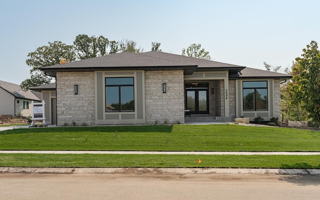 prairie-style house featuring stone siding, french doors, a shingled roof, and a front lawn