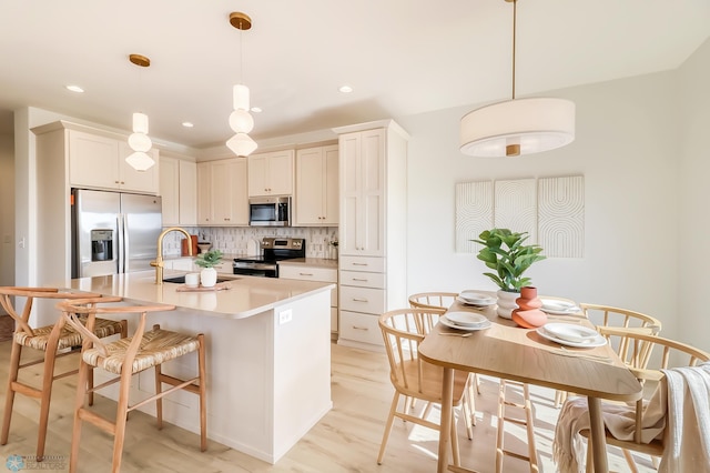 kitchen featuring an island with sink, a sink, backsplash, stainless steel appliances, and light countertops