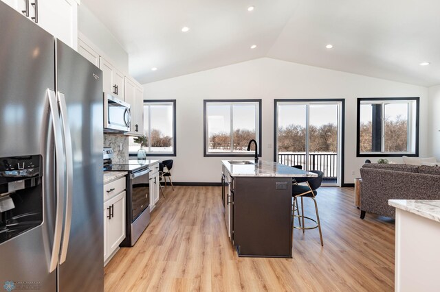 kitchen featuring vaulted ceiling, white cabinetry, stainless steel appliances, and a sink