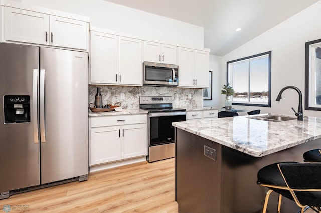 kitchen with a kitchen bar, lofted ceiling, white cabinets, stainless steel appliances, and a sink