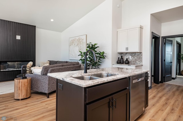 kitchen with light stone counters, an island with sink, a sink, stainless steel dishwasher, and tasteful backsplash