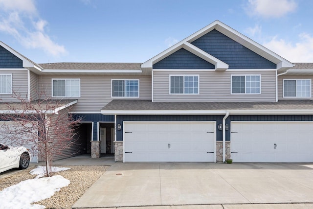 townhome / multi-family property with stone siding, a garage, and driveway