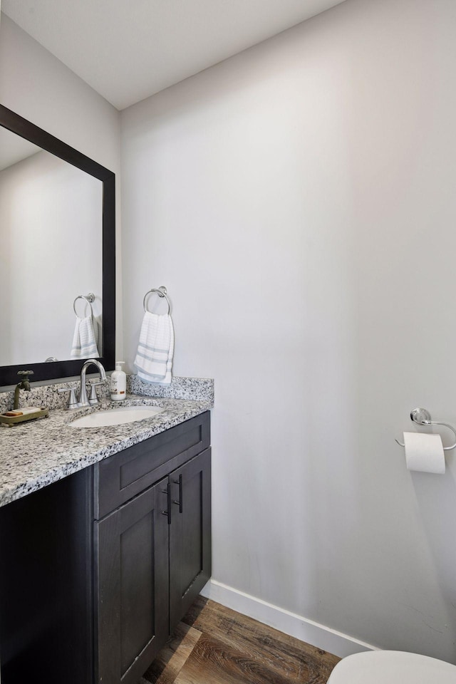 bathroom with vanity, toilet, wood finished floors, and baseboards