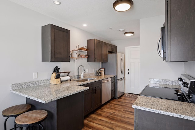 kitchen with open shelves, a sink, stainless steel appliances, dark brown cabinetry, and a kitchen bar