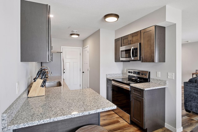 kitchen featuring dark brown cabinets, appliances with stainless steel finishes, light wood-type flooring, and a sink