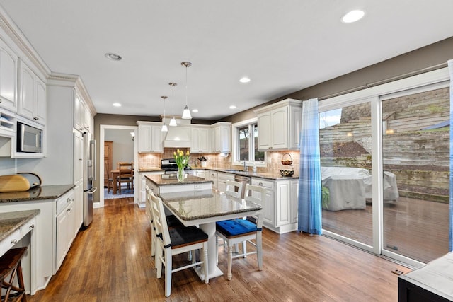 kitchen featuring stainless steel appliances, a kitchen island, wood finished floors, and decorative backsplash