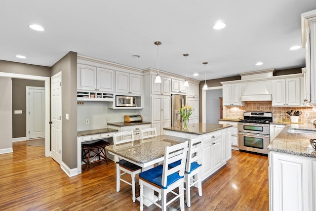 kitchen with a sink, a center island, appliances with stainless steel finishes, light stone countertops, and custom exhaust hood