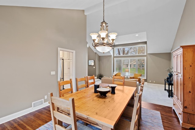 dining area featuring baseboards, visible vents, high vaulted ceiling, dark wood finished floors, and a chandelier