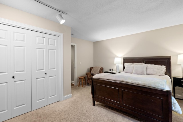 bedroom with baseboards, track lighting, a closet, a textured ceiling, and light carpet