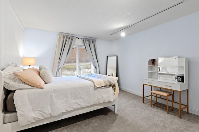 carpeted bedroom with rail lighting, a textured ceiling, and baseboards