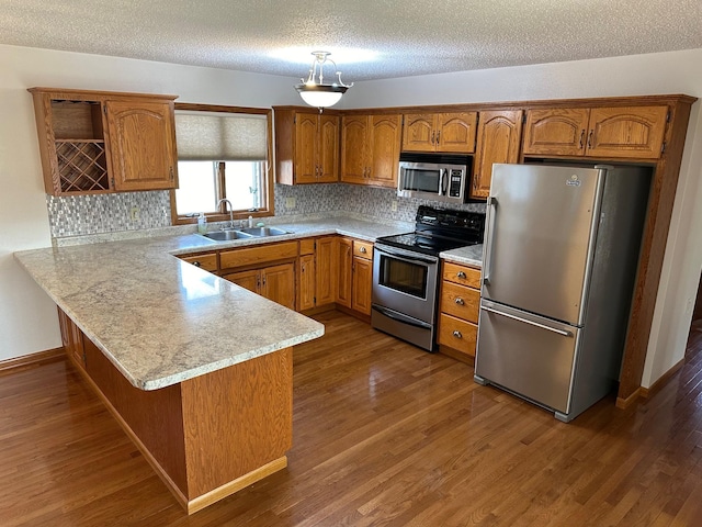 kitchen with a sink, stainless steel appliances, a peninsula, brown cabinetry, and light countertops