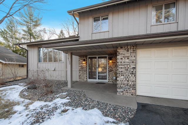 doorway to property featuring brick siding, board and batten siding, and an attached garage