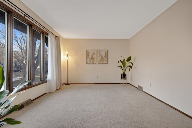 unfurnished room featuring plenty of natural light, light colored carpet, visible vents, and baseboards