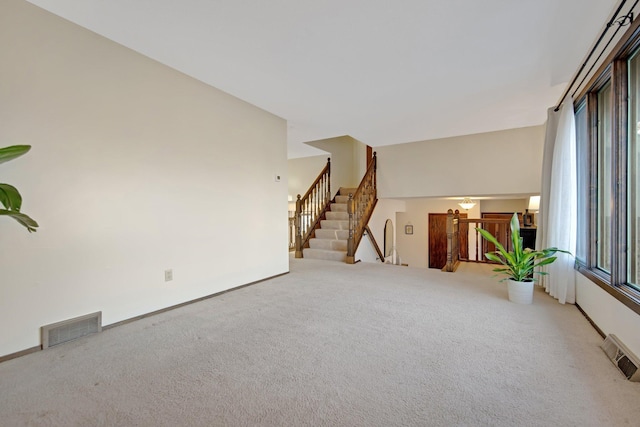 unfurnished living room with visible vents, baseboards, carpet, and stairway