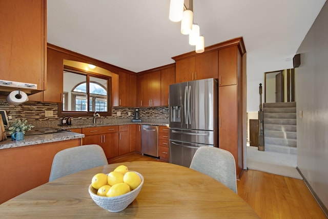 kitchen featuring light wood-type flooring, a sink, decorative backsplash, appliances with stainless steel finishes, and brown cabinets