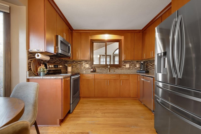 kitchen featuring tasteful backsplash, appliances with stainless steel finishes, light wood-style floors, and a sink