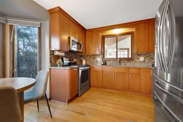 kitchen featuring light stone countertops, light wood-style flooring, decorative backsplash, appliances with stainless steel finishes, and brown cabinets