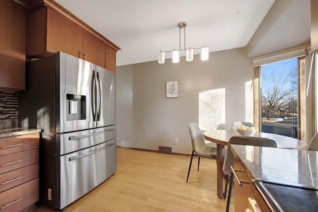 kitchen featuring light wood-type flooring, brown cabinets, pendant lighting, stainless steel refrigerator with ice dispenser, and decorative backsplash