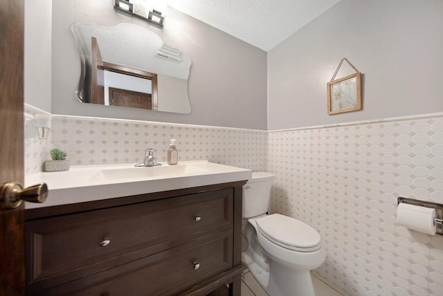 half bathroom featuring vanity, a textured ceiling, wainscoting, tile walls, and toilet