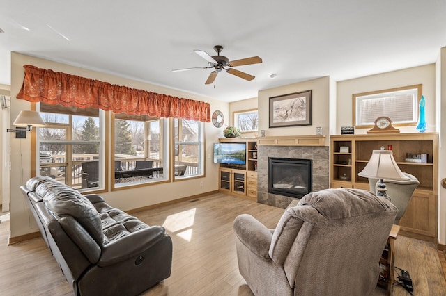 living room featuring light wood-style flooring, a fireplace, baseboards, and ceiling fan