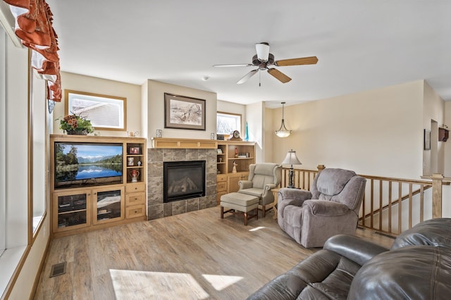 living area with a tiled fireplace, a healthy amount of sunlight, ceiling fan, and wood finished floors